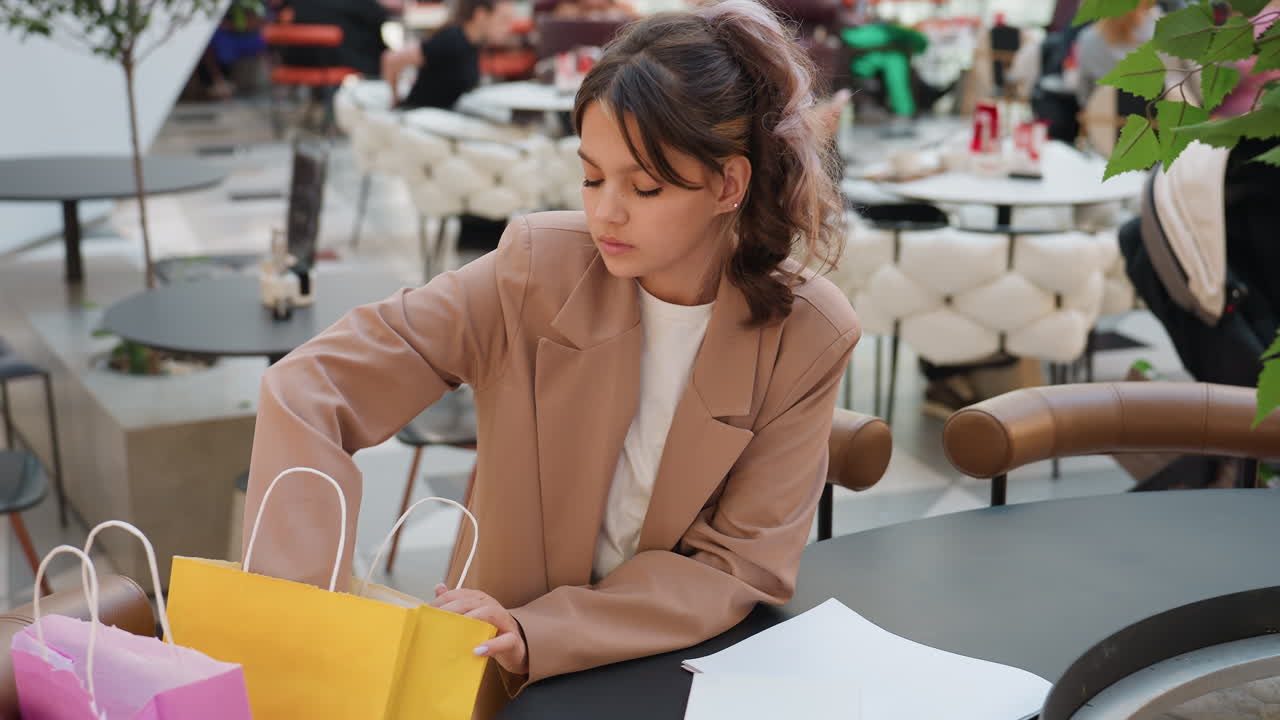 Una joven organiza los artículos que ha comprado de forma reflexiva; una compradora organiza los regalos y los recibos en los asientos del centro comercial; una joven organiza cuidadosamente los artículos que ha comprado y los recibos en un ambiente relajado del centro comercial.