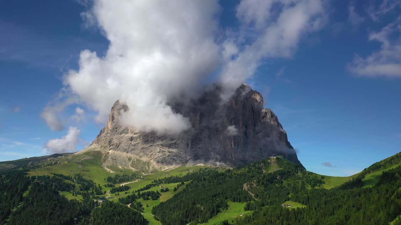 Clouds around Sassolungo mountain in the Dolomites in Italy, backward aerial