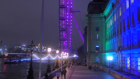 Ojo-De-Londres-En-La-Noche-Iluminado-Durante-La-Temporada-De-Navidad-En-La-Orilla-Sur-De-Londres-Con-Gente-Caminando-En-El-Paseo-Marítimo-En-Inglaterra,-Reino-Unido