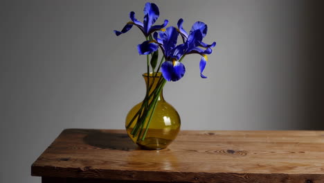 blue iris flowers in a yellow vase on a wooden table