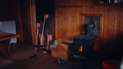 cropped view of a man sweeping the floor of a cabin with a fireplace. close-up shot