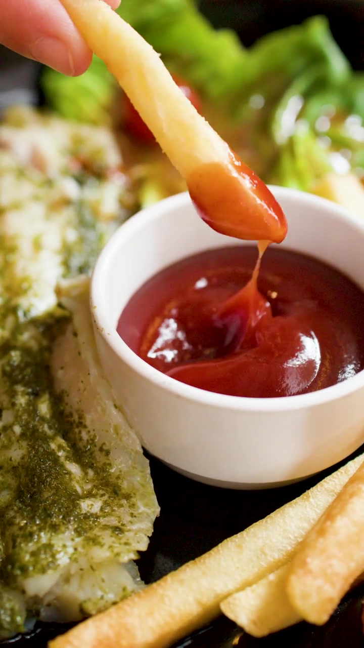 Eine Person taucht eine goldene Pommes frites in eine Schale mit roter Tomatenketchup-Soße.