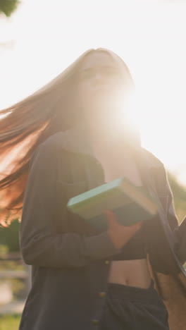 dama alegremente gira al aire libre en el campo de hierba con un libro en la mano, la luz del sol que irradia a su alrededor, la creación de una atmósfera brillante, el fondo cuenta con vegetación, árboles, y un ligeramente borroso