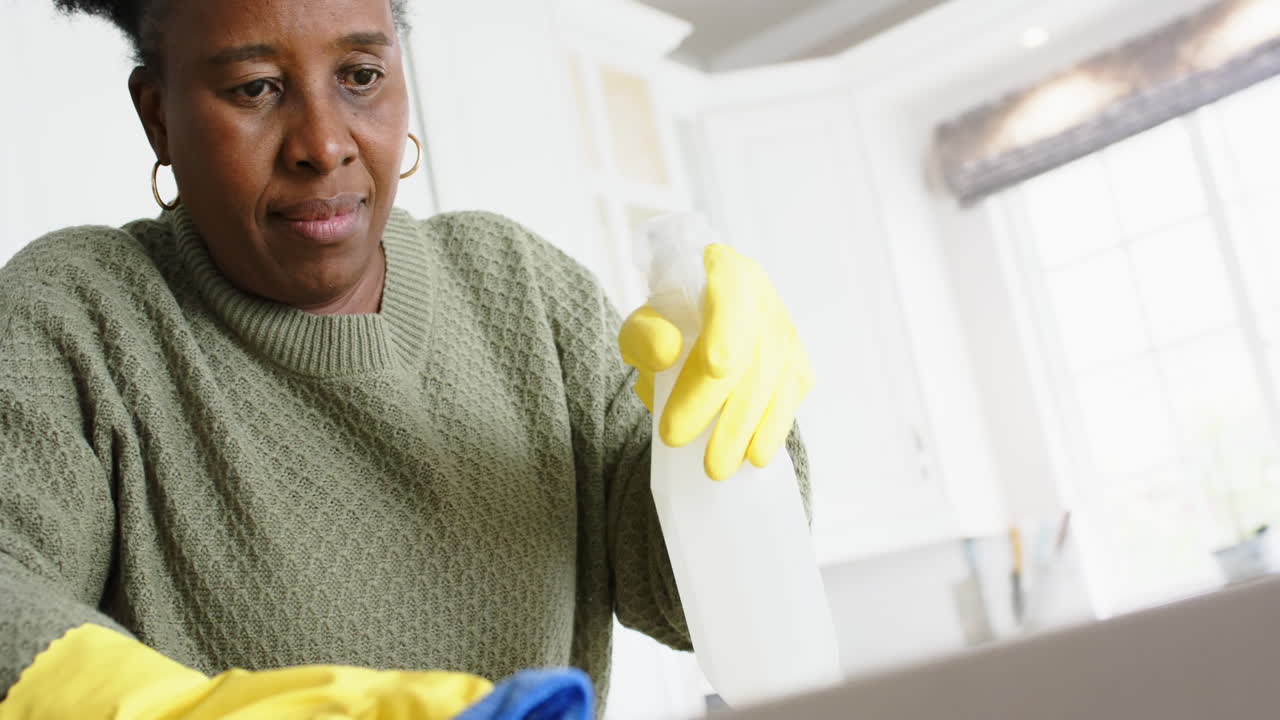 Happy african american senior woman cleaning counter and smiling in sunny kitchen, slow motion
