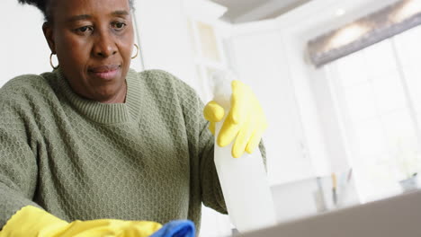 Feliz-Mujer-Mayor-Afroamericana-Limpiando-Mostrador-Y-Sonriendo-En-Cocina-Soleada,-Cámara-Lenta