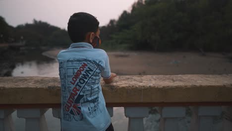 a young boy excited climbing up onto a stone bridge looking over to spot fish and other creatures along the bank of the mandovi river at sunset, goa, india