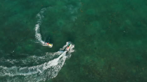 Jet-ski-riders-enjoying-their-time-while-cruising-on-the-calm-sea-surface.-Aerial-Birds-Eye-Overhead-Top-Down-View,-rotating-counterclockwise