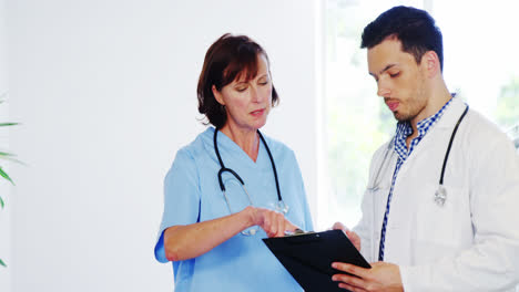 Nurse-and-doctor-discussing-over-clipboard-in-corridor