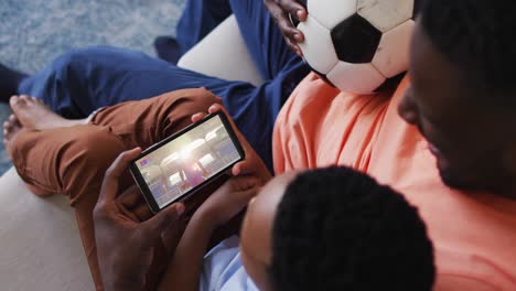 Compuesto-De-Padre-E-Hijo-En-Casa-Viendo-Un-Evento-Deportivo-En-Un-Teléfono-Inteligente