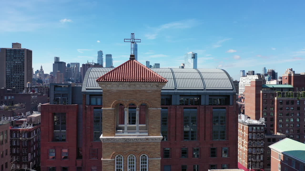 an aerial view of the bell tower of a church in Greenwich Village, NYC. The camera orbits counterclockwise around the red roof tower on a sunny morning. The Freedom Tower is in the distance.
