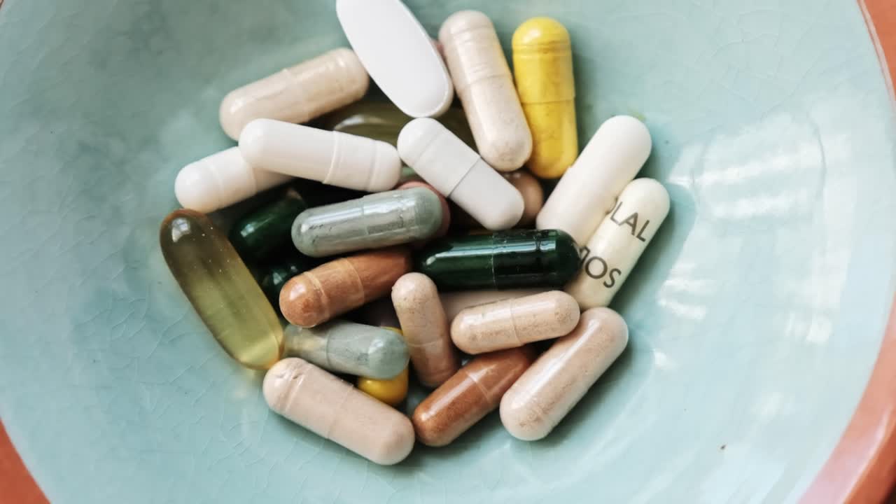A blue ceramic bowl full of supplements in capsule and tablet form as seen from above