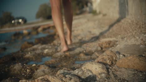 low angle of woman shoeless legs walking on stony beach