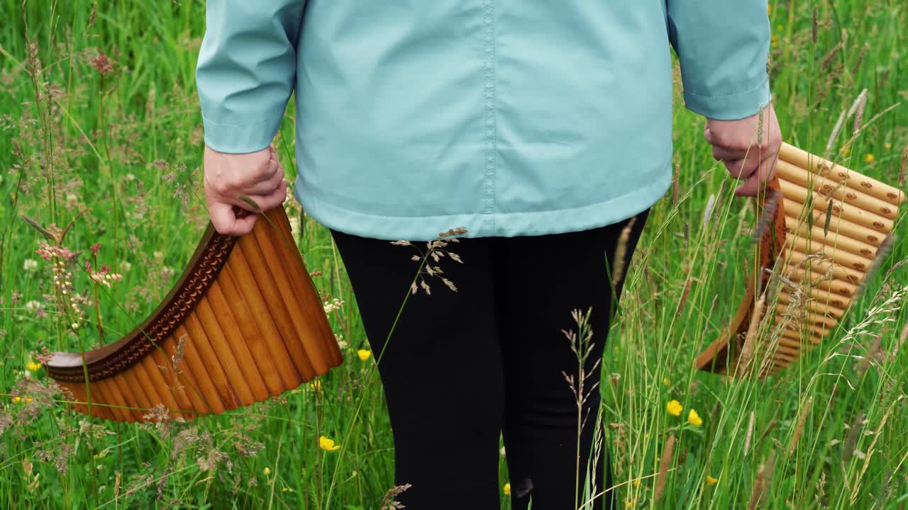 한 젊은 여성이 자연 속에서 두 개의 팬 플루트를 휘두른다