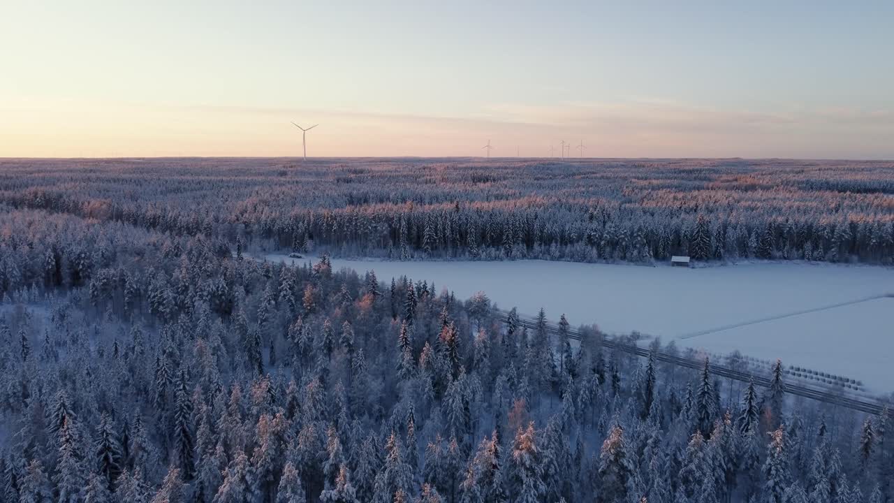일몰 동안 눈 덮인 숲에 여러 개의 풍력 터빈