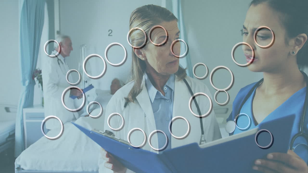 Senior doctor and nurse reviewing chart with stethoscope in medical room, showing animated data