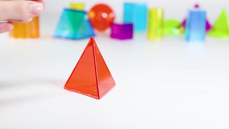a hand interacts with vibrant 3d geometric shapes on a white background, highlighting educational and playful elements