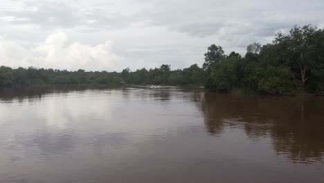 Slow-motion-aerial-view-of-a-traditional-speedboat-getting-closer-to-the-deck,-in-a-calm-river-in-the-middle-of-the-rainforest