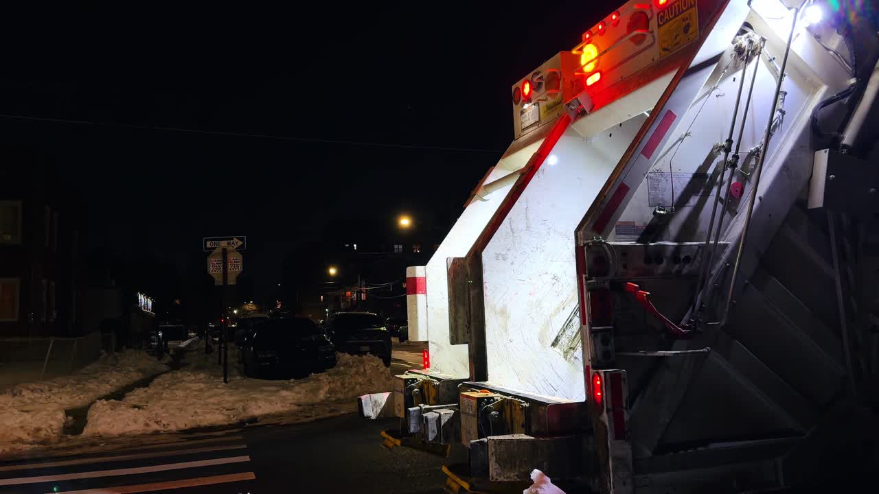 Nova York, EUA, 9 de fevereiro de 2026: Vista traseira de caminhão de lixo em rua nevada à noite. Veículo de saneamento estacionado em uma rua residencial escura com neve e uma placa de sentido único