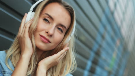 close-up view of blonde young woman listening to music with headphones and singing in the street