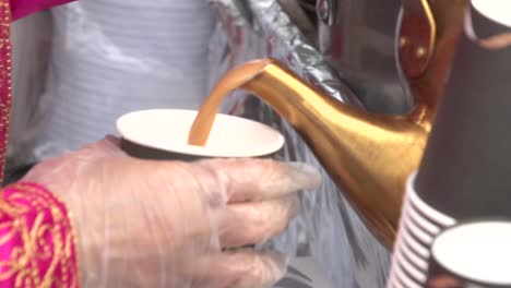 karak tea being poured from an arab traditional tin tea pot into a paper cup