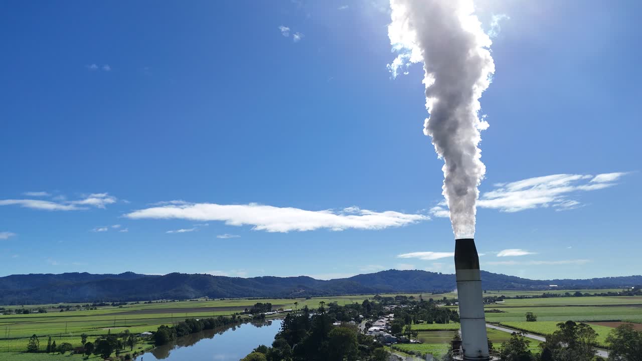 Aerial footage of a cooling tower emitting steam beside a river, under clear blue skies, showcasing industrial and natural landscapes