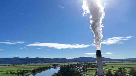 aerial footage of a cooling tower emitting steam beside a river, under clear blue skies, showcasing industrial and natural landscapes