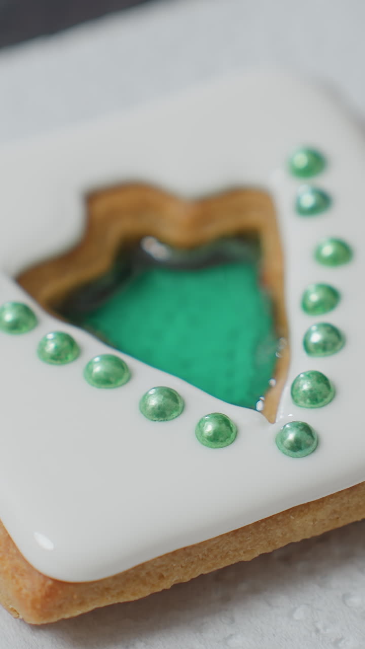 primer plano de una galleta hermosamente decorada con glaseado blanco y adornos de perlas verdes colocados en papel de pañuelo, la galleta tiene un centro cortado lleno de un diseño verde brillante