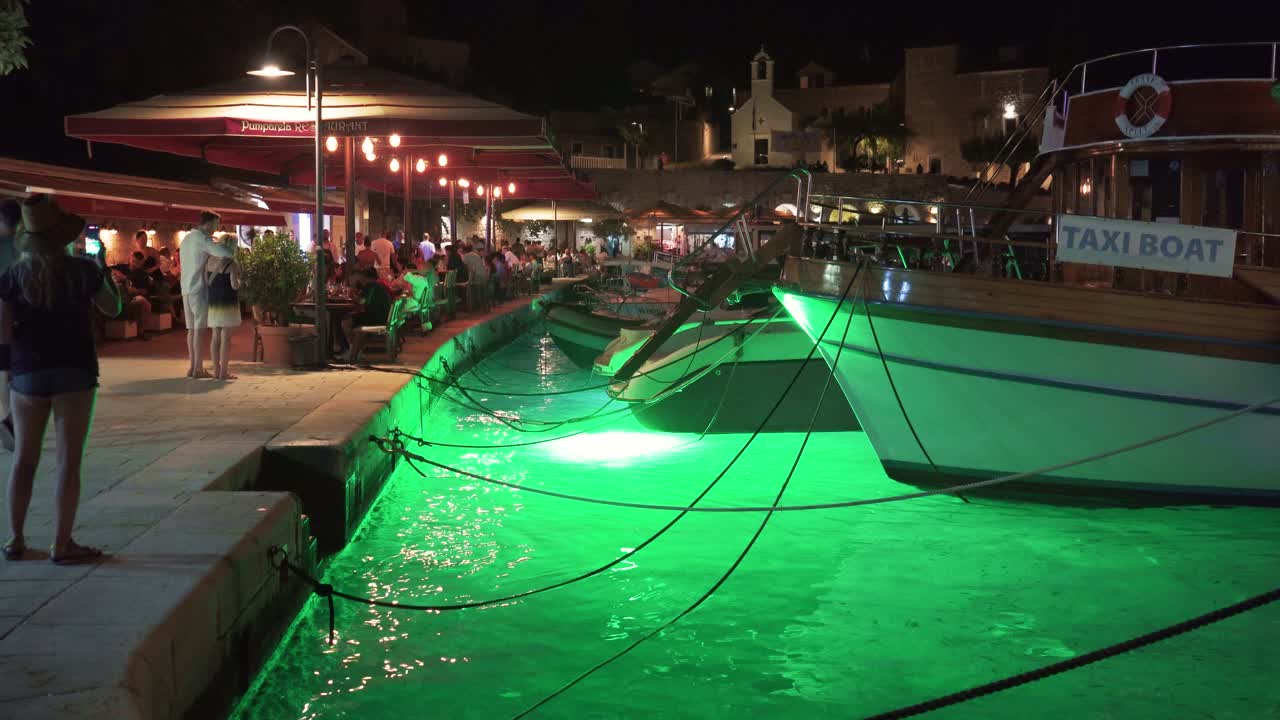 Evening View at Famous Torurist Resort Bol on Island Brac, Croatia Mediterranean Coastal Adriatic City of Bol, Tourists at Bars Party Cruise Sailboats and Traditional Fishing Boats Docked in Harbor