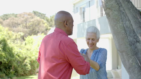 Feliz-Pareja-Birracial-Mayor-Bailando-En-El-Soleado-Jardín-De-Casa,-Cámara-Lenta