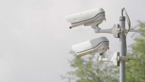 Rack-Fokus-Auf-Weiße-CCTV-Kameras,-Die-Auf-Metallpfosten-Montiert-Sind,-Nahaufnahme