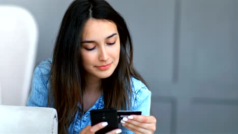 joven bonita comprando en línea con tarjeta de crédito y teléfono inteligente acostado en un sofá en la sala de estar en casa