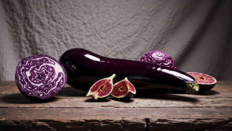 still life of purple eggplant, red cabbage, and figs on wood