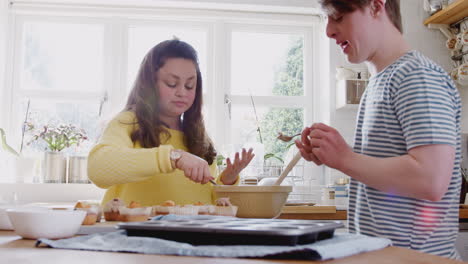 Junges-Down-Syndrom-Paar-Dekoriert-Hausgemachte-Cupcakes-Mit-Zuckerguss-In-Der-Heimischen-Küche