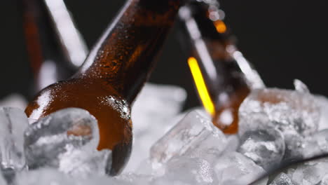 cerrar las botellas de vidrio de cerveza fría o refrescos que se enfrían en un cubo lleno de hielo contra un fondo negro 1