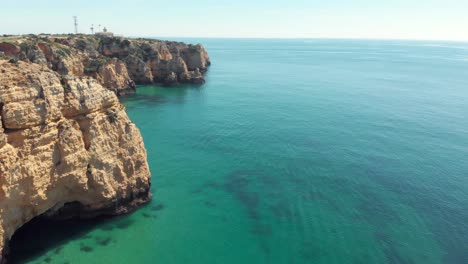 Vast-turquoise-ocean-bared-by-Steep-eroded-cliffs-in-Lagos-coast,-Algarve,-Portugal---Aerial-fly-by-slow-tilt-up-reveal-tracking-shot