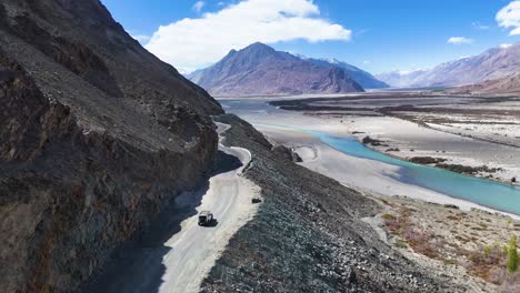 aerial drone shot capturing the contrast between a moving car and the flowing river cutting through nubra valley’s terrain.