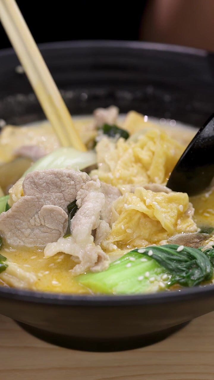 Primo piano di bacchette e cucchiaio che sollevano una zuppa di noodle asiatica piccante in un'illuminazione calda