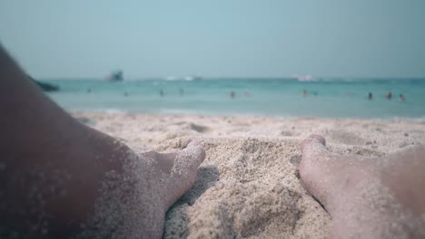 Mann-Mit-Behaarten-Beinen-Im-Sand-Am-Gelben-Strand-In-Der-Nähe-Des-Ozeans,-Nahaufnahme