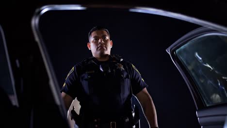an officer stands guard next to a parked vehicle during a night patrol. the area is dimly lit, highlighting the officer's presence as they ensure safety and security.