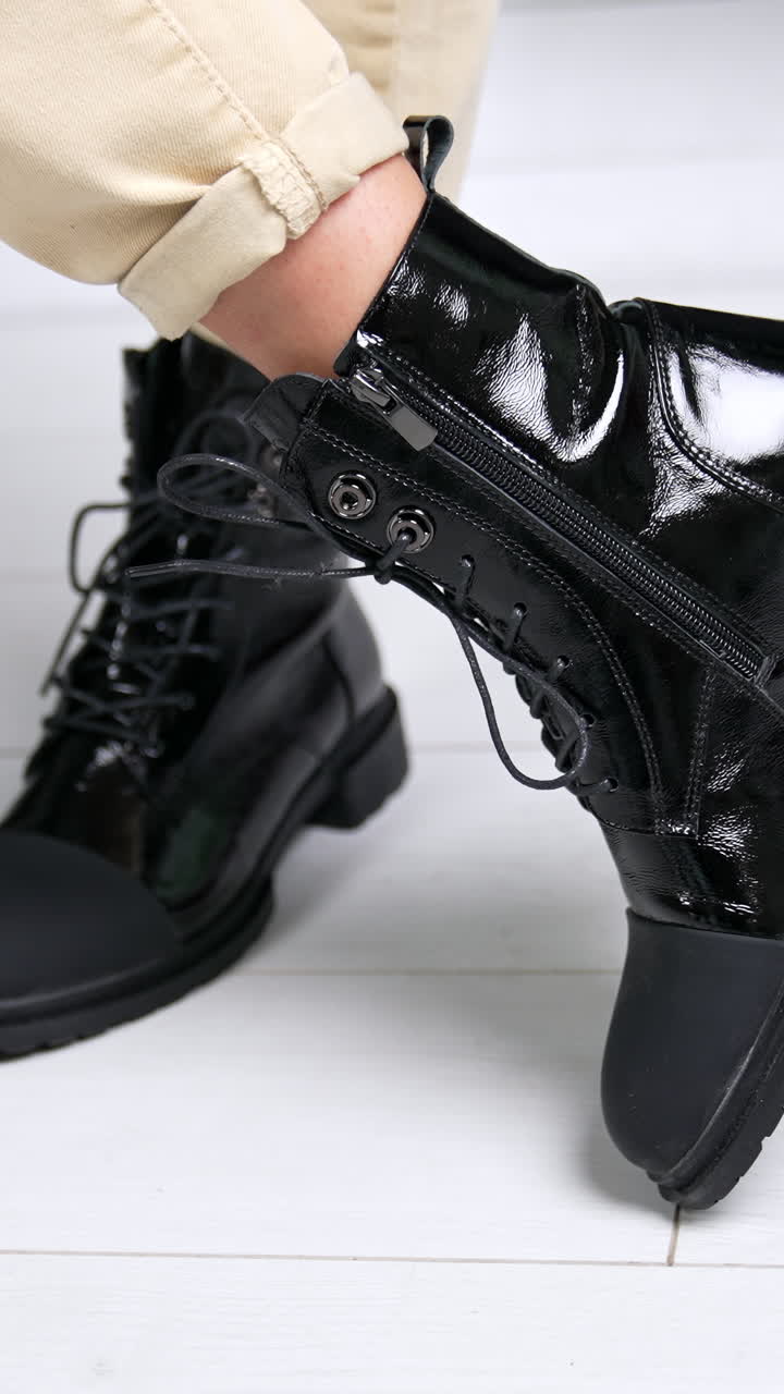 Female wearing black lacquered boots with opaque nosepieces. Model stands and turns around in her comfortable stylish footwear. Close up. Vertical video