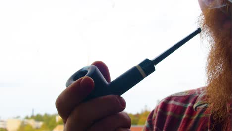 un hombre de barba roja probando su nueva marca de tabaco que acaba de comprar para su pipa negra para fumar a la antigua usanza cuando los vaqueros todavía estaban aquí día nublado con nture en el fondo