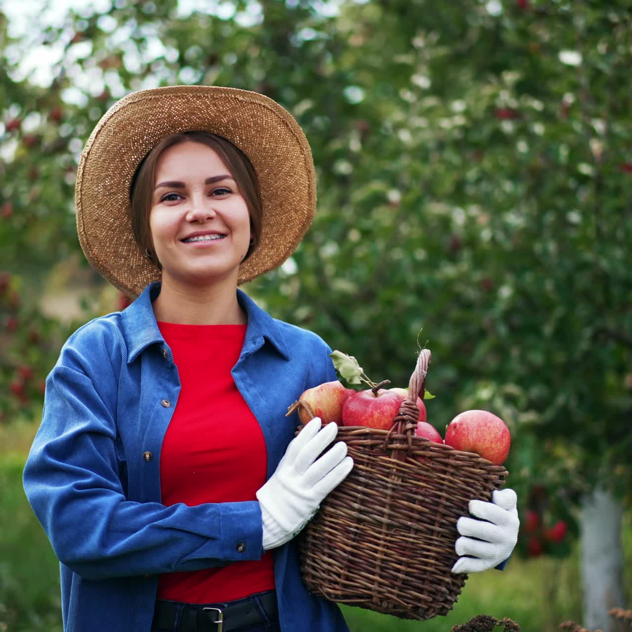 Caucasian lady is happy about the harvest of apples collected in the garden. Woman in hat holds a full basket of fruit standing in the orchard