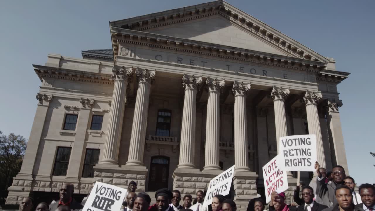 Ripresa video dal basso verso l'alto di un tribunale neoclassico con colonne, che cattura cartelli di protesta a sostegno di