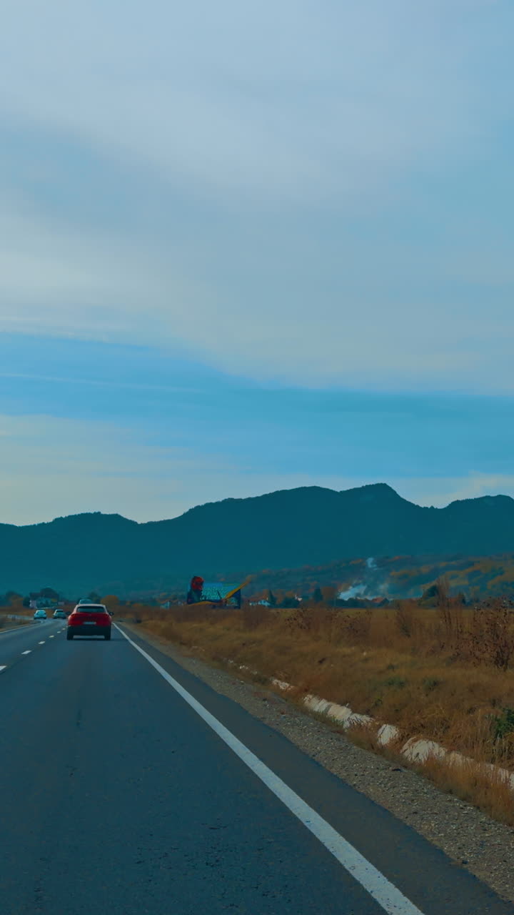 Driving by the speedway through the valley. Silhouette of mountain range at backdrop. Vertical video