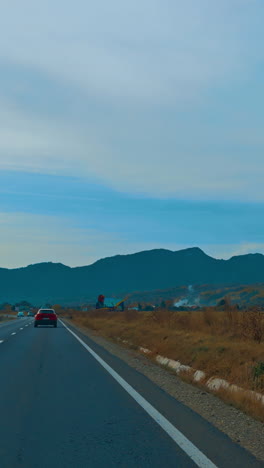 driving by the speedway through the valley. silhouette of mountain range at backdrop. vertical video