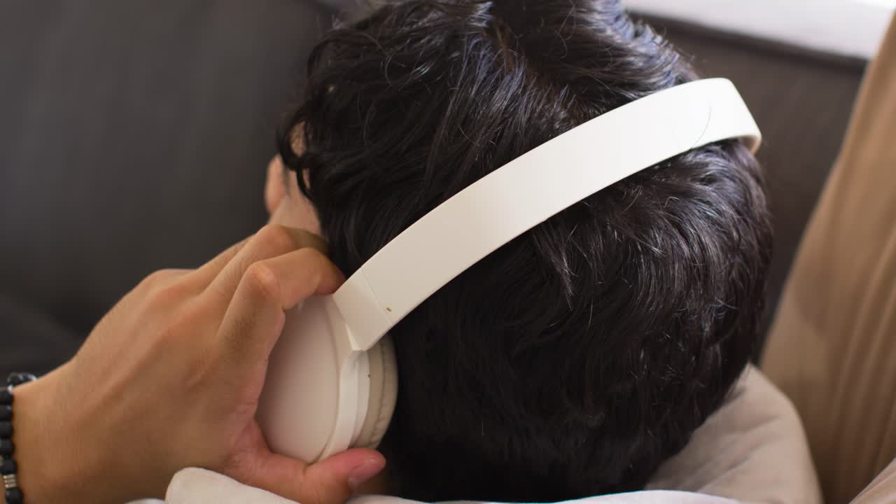 白いヘッドホンを手に取り、イヤーカップの位置を合わせ、音声のためにフィット感を調整している成人男性。