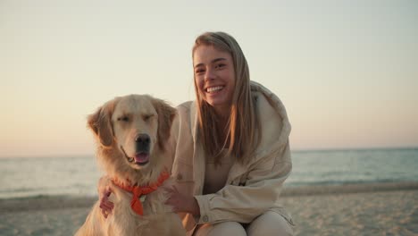 portrait of a young blonde girl petting her dog and looking at the camera in the morning on the seashore