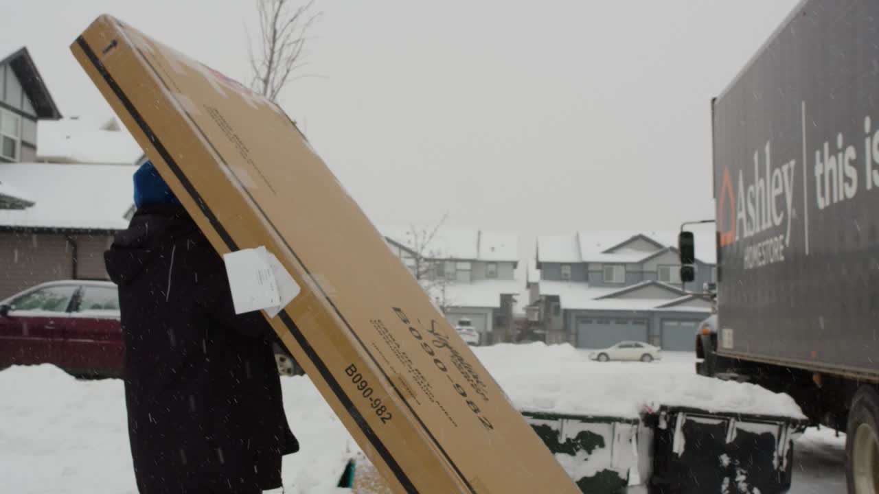 Tracking shot delivery man struggling with box from truck home snowing winter neighborhood