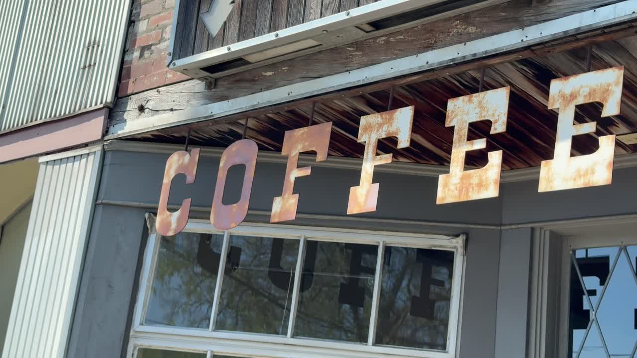 Rustic, rusting coffee cafe sign hanging above the entrance of a ghost town store - isolated street view and panning reveal
