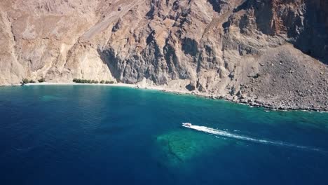 Small-Boat-Approaches-Exotic-Beach-Under-Huge-Cliff-In-South-Crete,-Greece